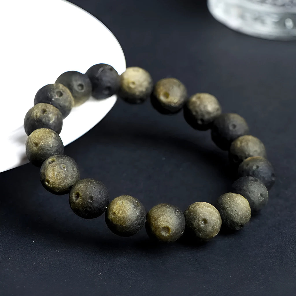 Obsidian crater ball bracelet on a wrist, showing ground stone texture and bead size.