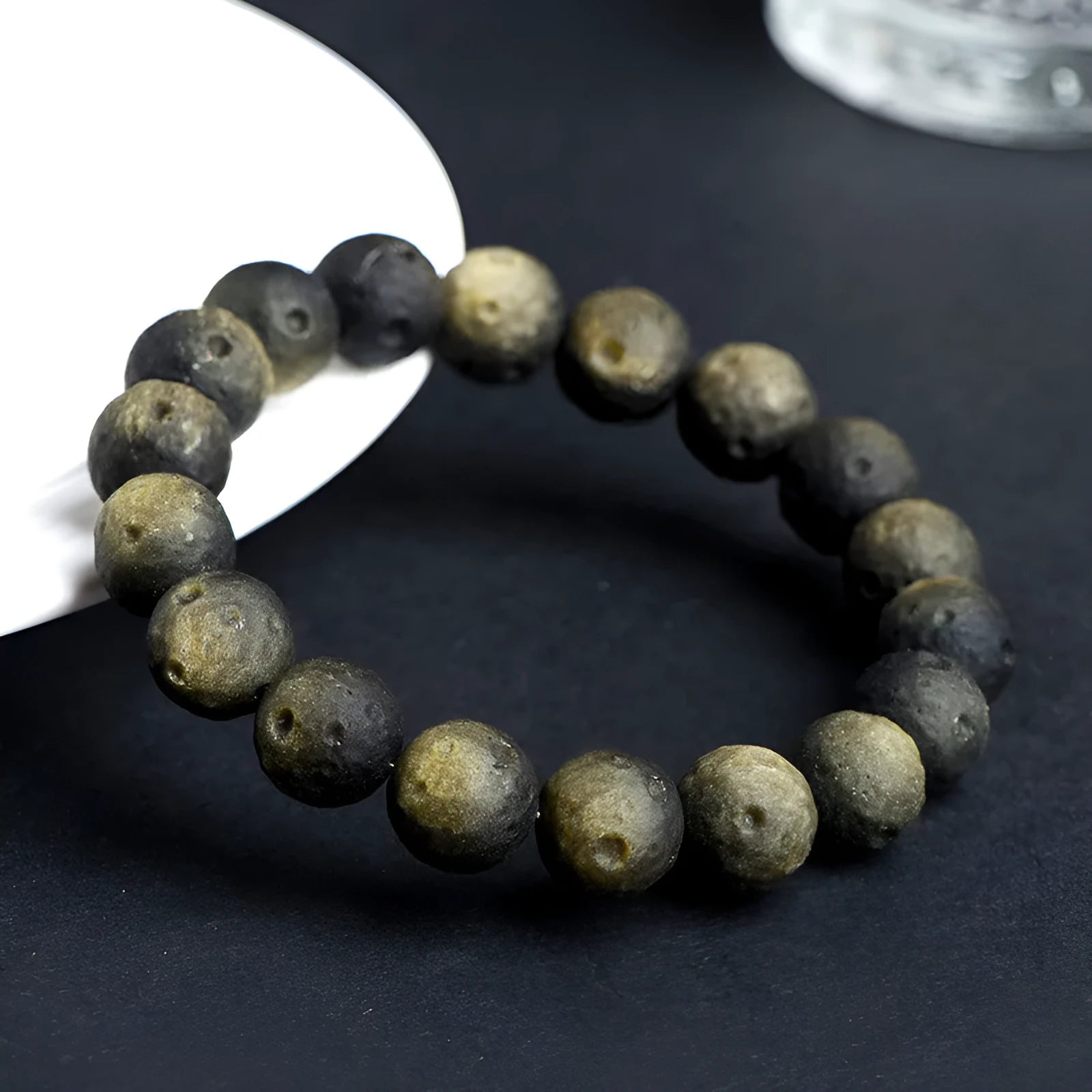 Obsidian crater ball bracelet on a wrist, showing ground stone texture and bead size.