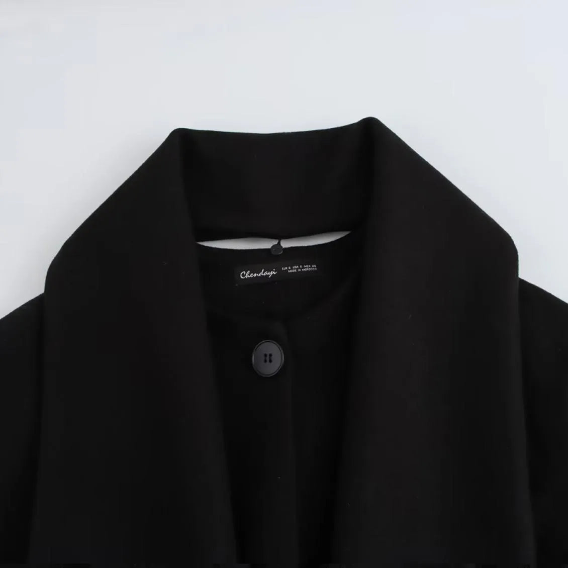 Women's long black coat with a grey artificial fur collar and side pockets, shown in a street fashion setting.