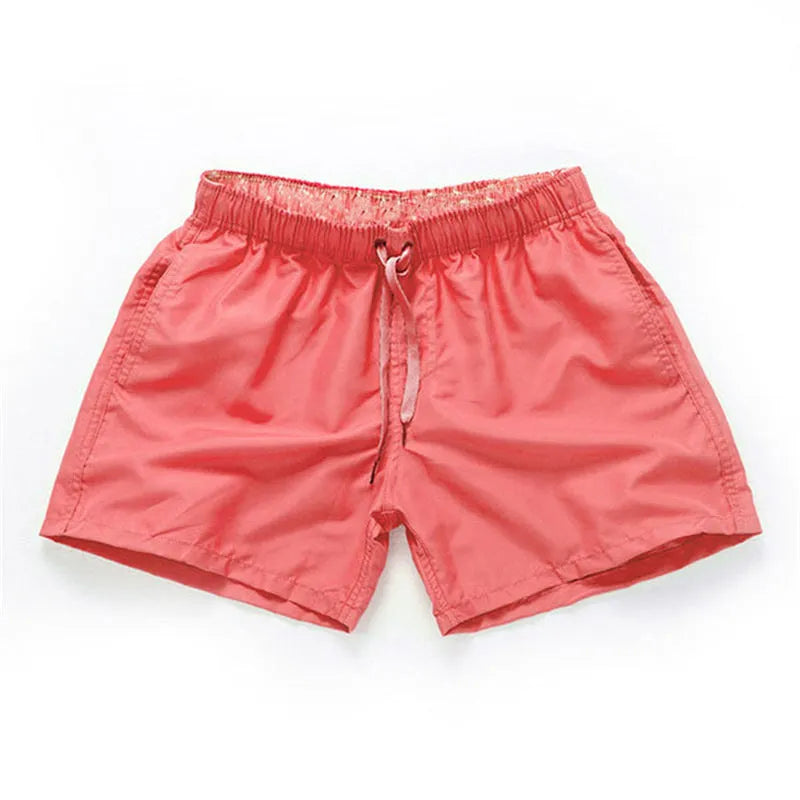 Men's straight-leg polyester surf shorts on a beach, showing colour options like black, fluorescent yellow, and navy blue.