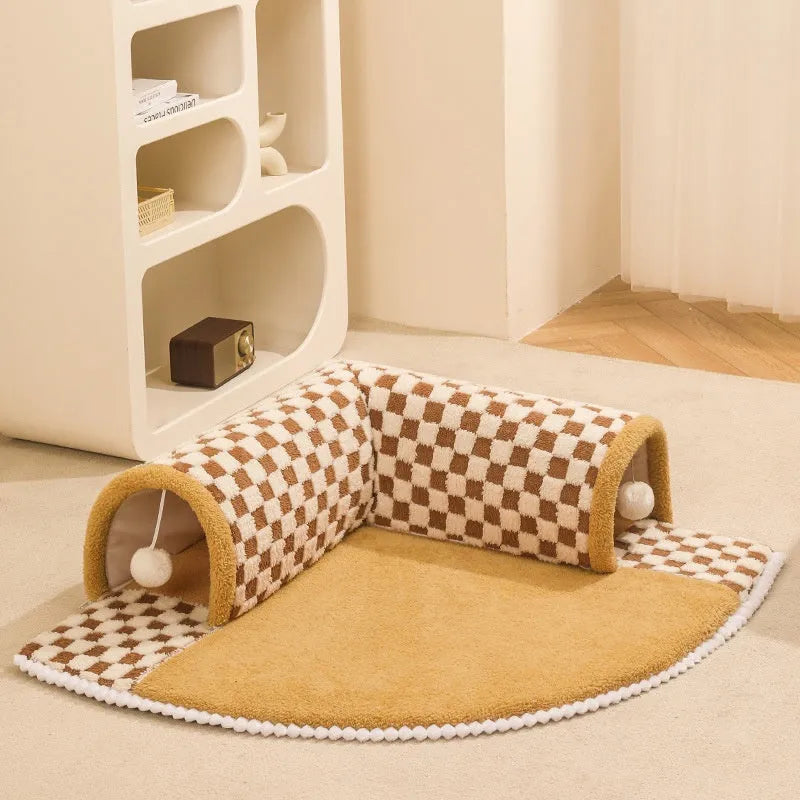 Brown plush plaid cat tunnel bed with a central mat, shown on a wooden floor.