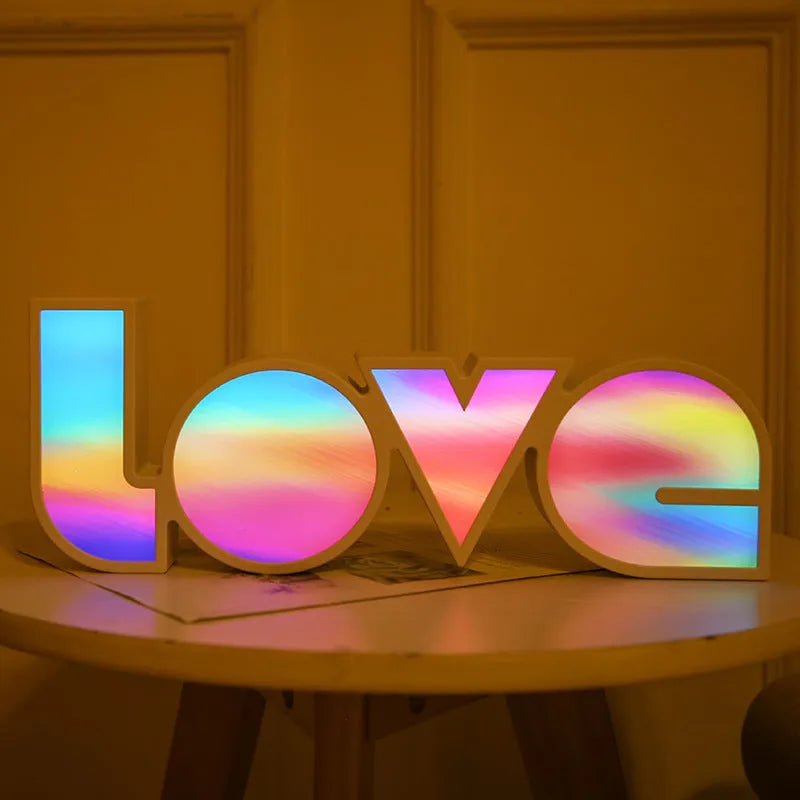 LED LOVE light with rainbow-coloured plastic shade on a desk.