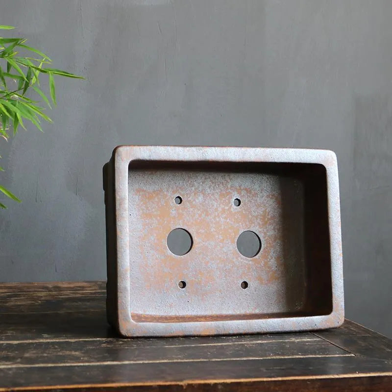 Rectangular purple sand bonsai pot with burnt pine tree decoration, shown on a garden surface.