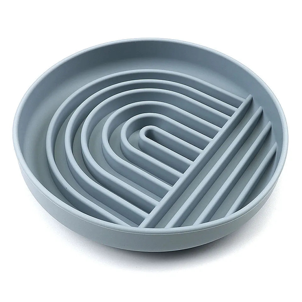Beige silicone dog slow feeder bowl with ridges, shown next to a grey blue version on a wooden floor.