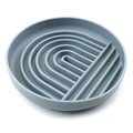 Beige silicone dog slow feeder bowl with ridges, shown next to a grey blue version on a wooden floor.