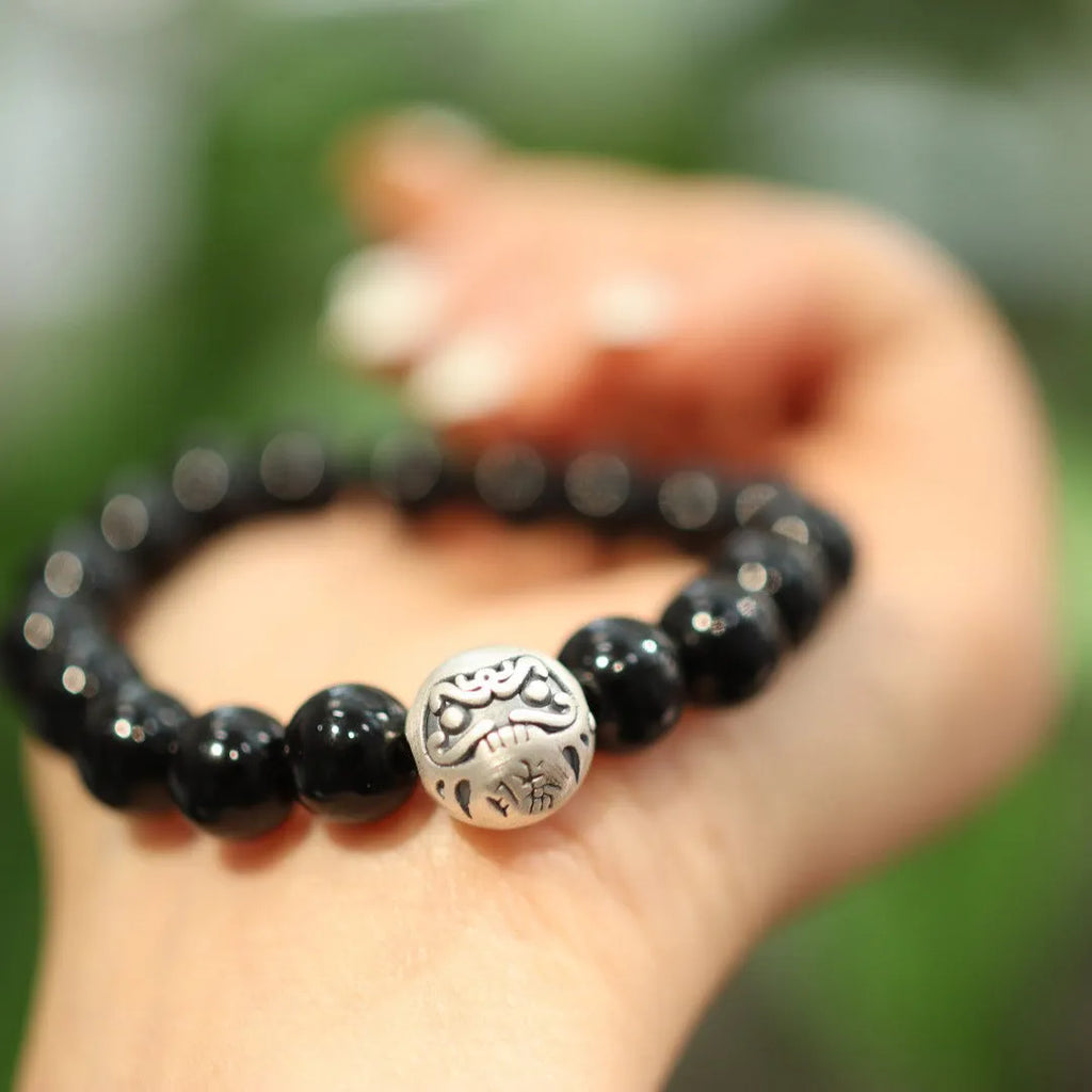 Close-up of a women's bracelet with large black agate beads and a sterling silver clasp on a wrist.