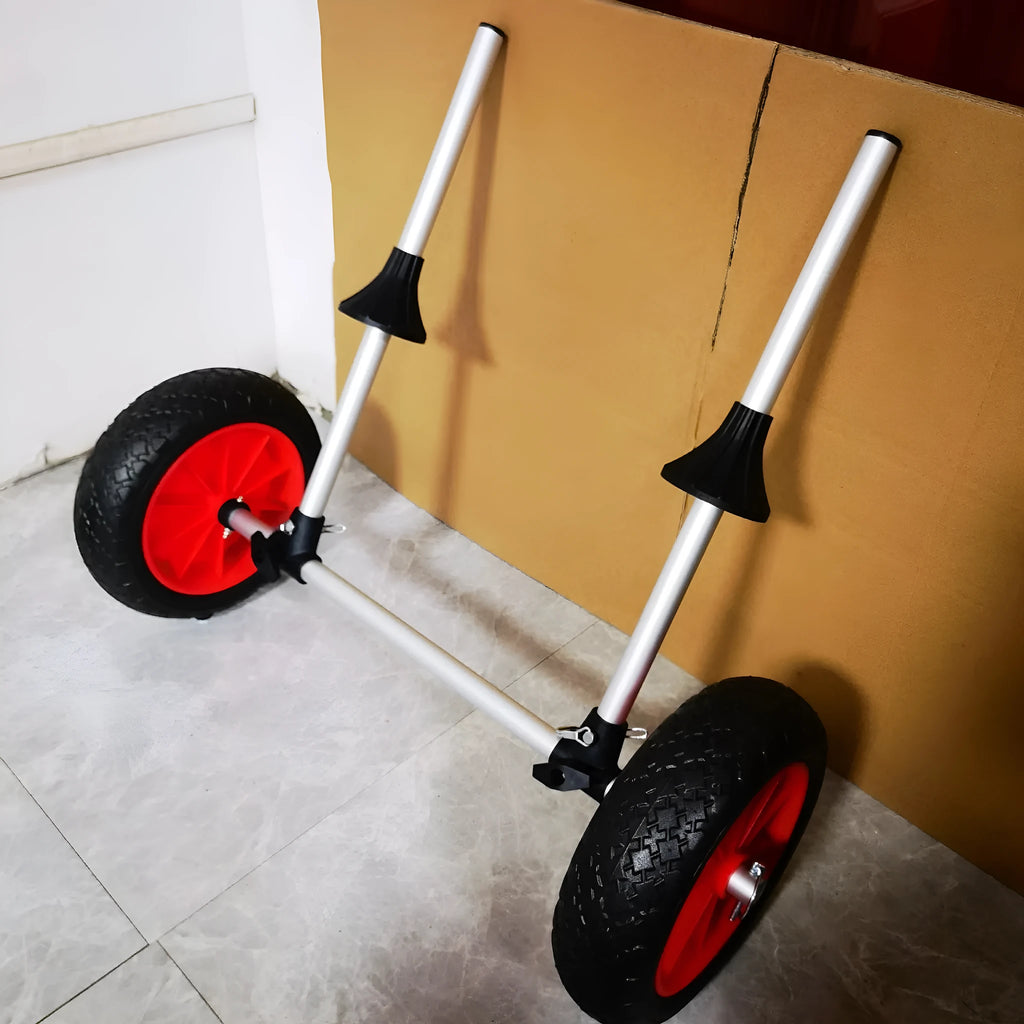 Foldable aluminium kayak beach trolley with solid rubber tyres, shown carrying a blue kayak on sand.
