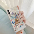 White iPhone case with a cartoon bear design and a connected silver bear pendant on a chain.