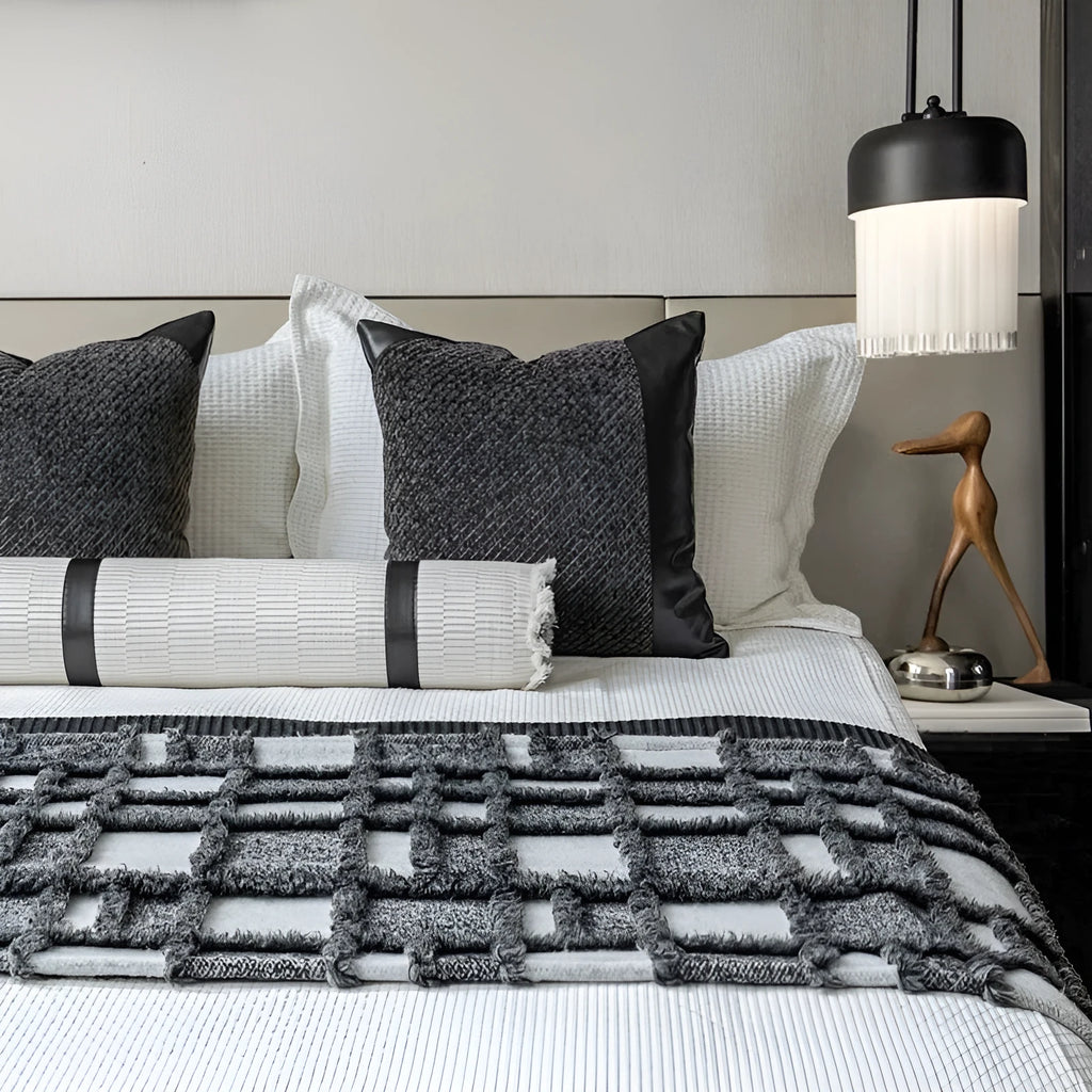 Grey and white plaid bed blanket draped over a dark grey duvet with a matching pillowcase and round leather-look cushion.