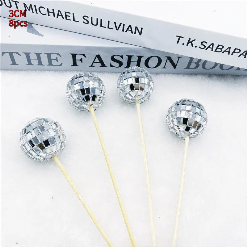 Glass disco ball cake decoration on a wooden stick in various sizes on a cake.