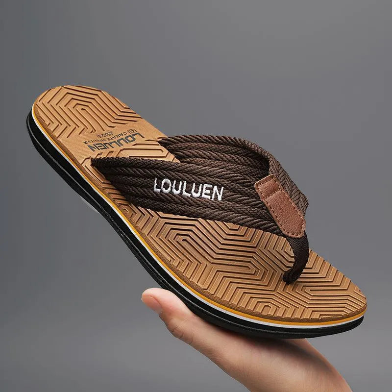 Men's black flip flops with open toe design and textured non-slip sole on a sandy beach.