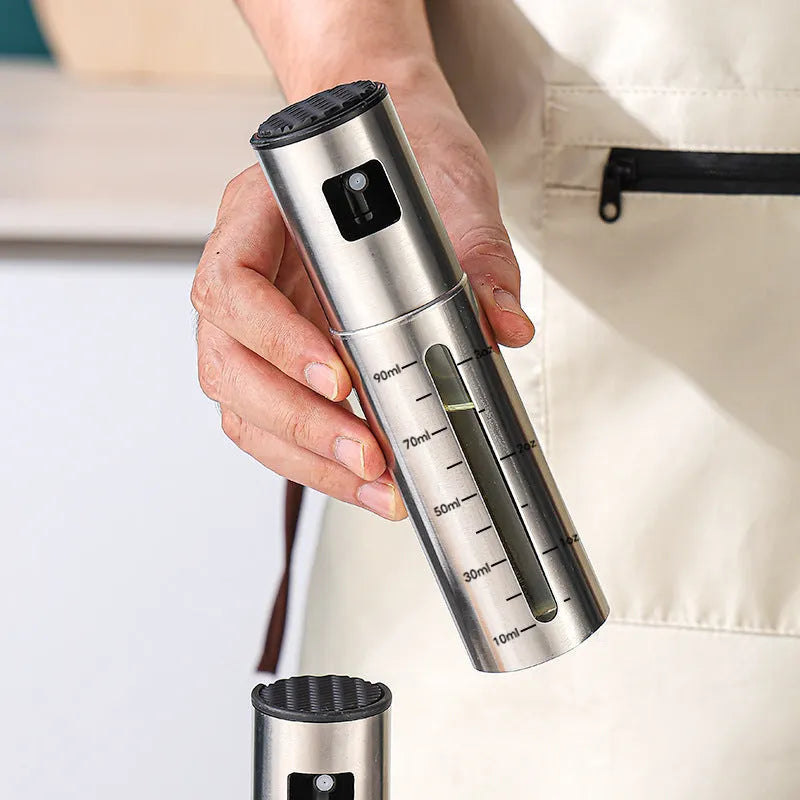 Stainless steel press spray oil injection bottle with glass body and 100ml capacity on kitchen countertop