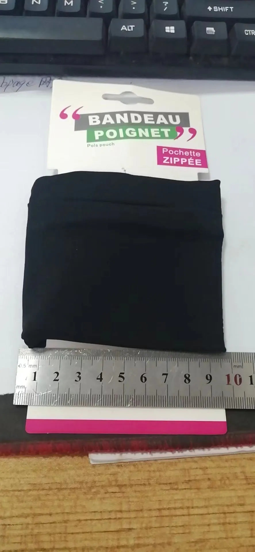 Black adjustable wrist bag with armband, showing zipped main compartment and external card slot on a person's forearm.