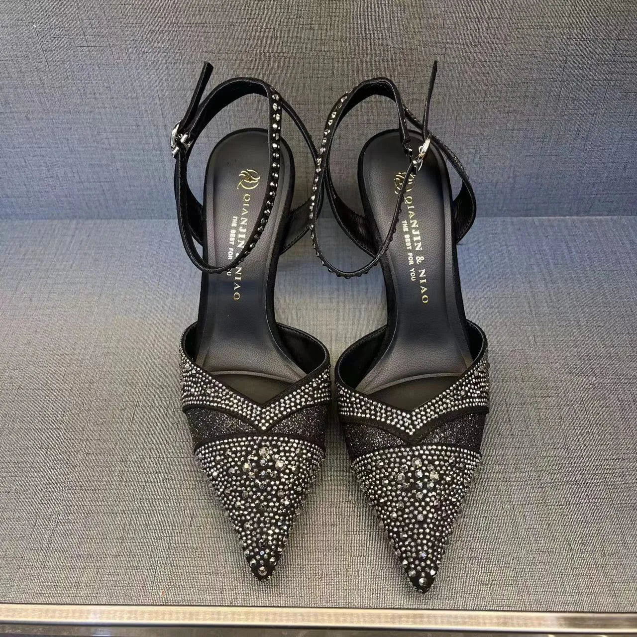 Women's black hollow high heel shoe with red sole, stiletto heel, and pointed toe on a plain background.