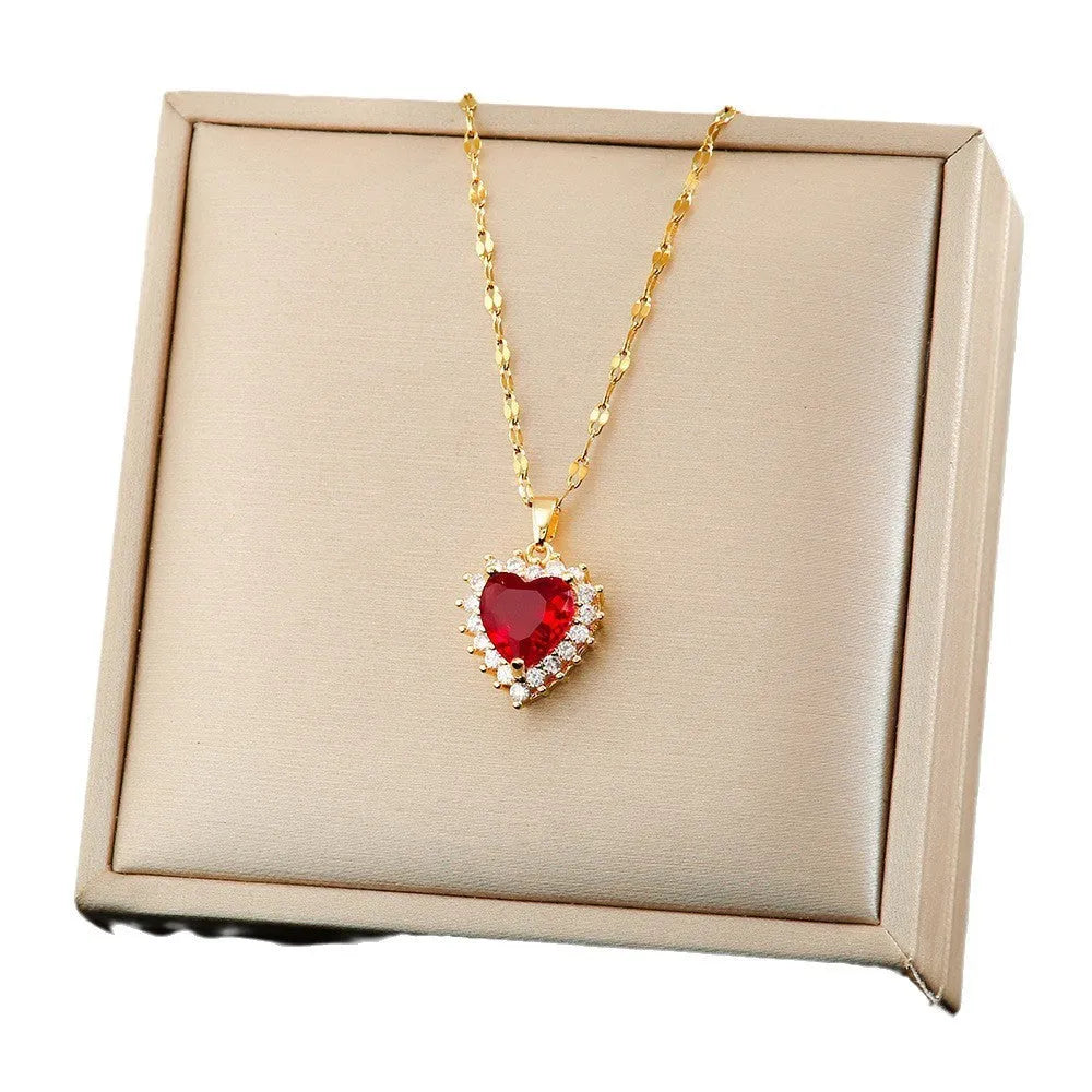 Gold red titanium steel necklace with heart and flower gem inlay pendant, matching stud earrings, and ring on a textured background.