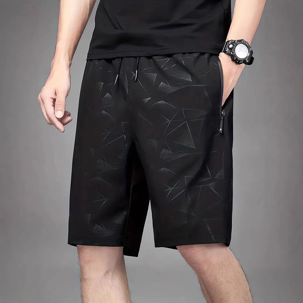 Man wearing loose black printed sports shorts on a beach.