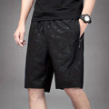 Man wearing loose black printed sports shorts on a beach.