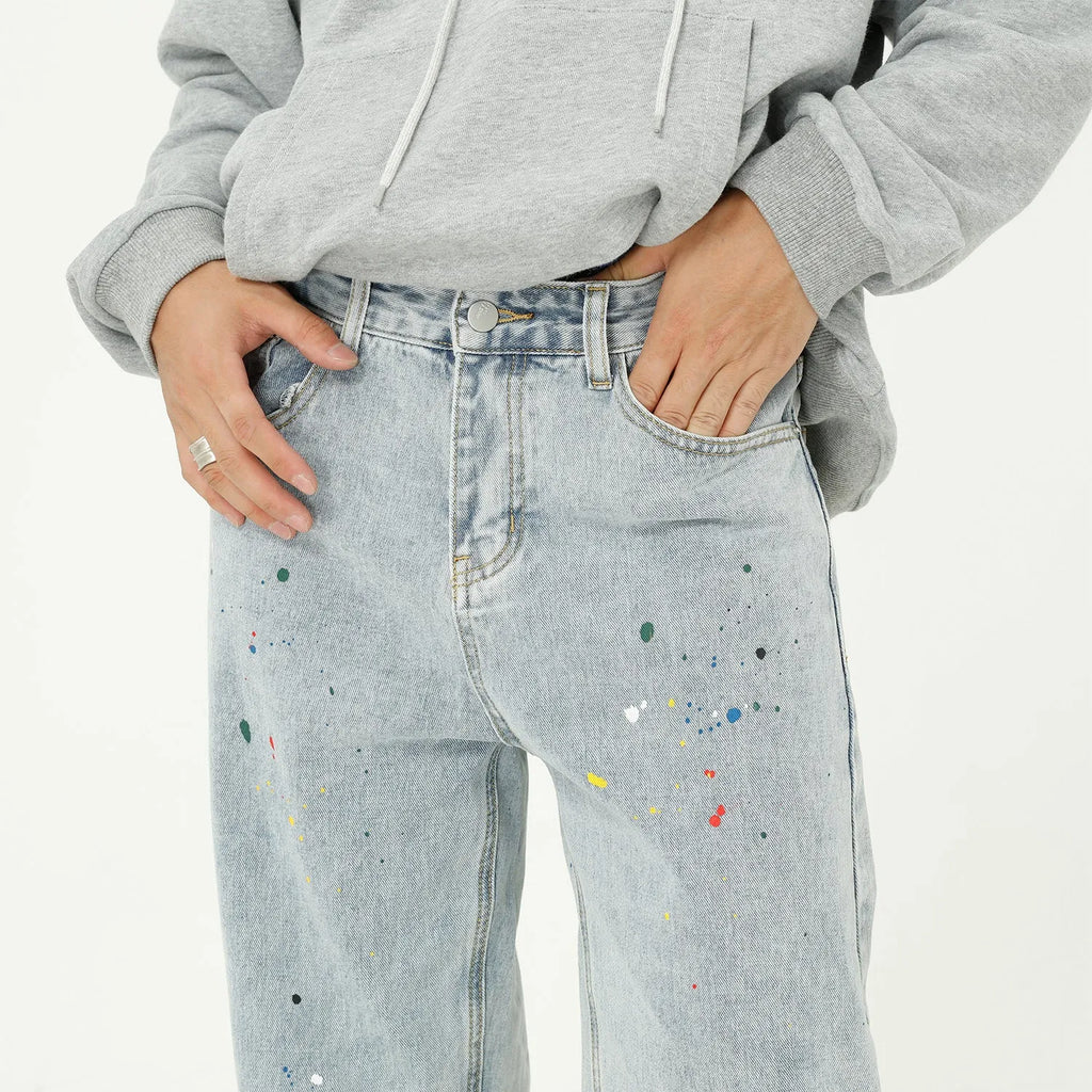 Light blue straight loose jeans with paint splash and washed finish, mid-waist zip fly, laid flat on neutral background