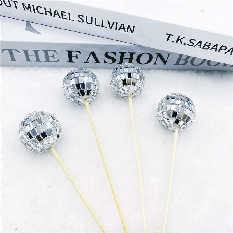 Glass disco ball cake decoration on a wooden stick in various sizes on a cake.