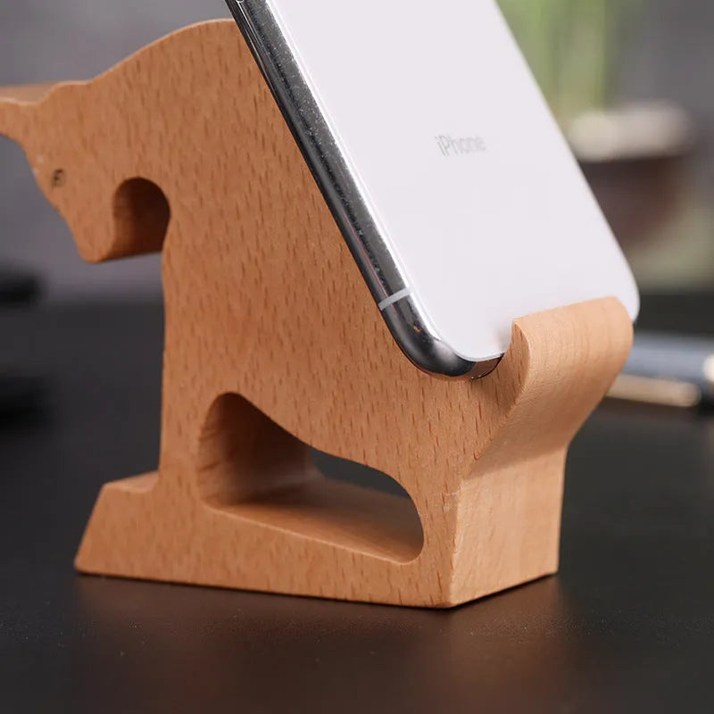 Solid beech wood mobile phone stand with a resin cow figurine and a slot for holding coins on a wooden desk.