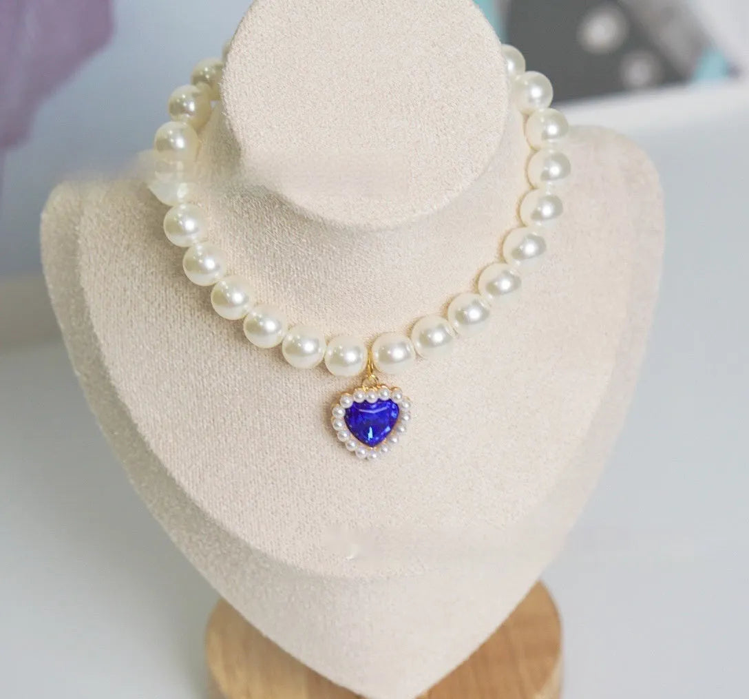 Pearl necklace cat collar with heart-shaped gem charm in various colours on a white background.