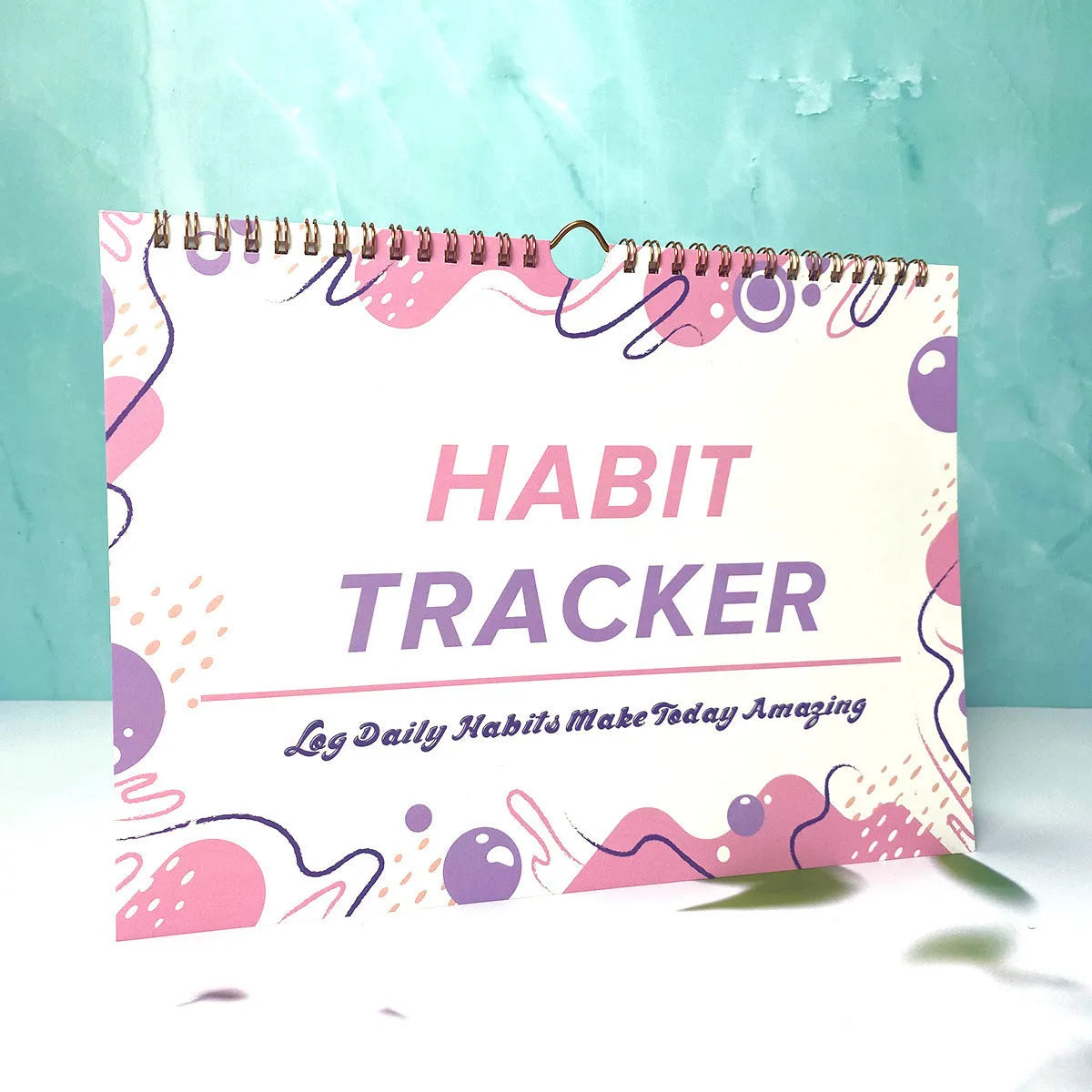 A5 habit tracking notebook open on a desk, showing internal pages, available in four colour options.