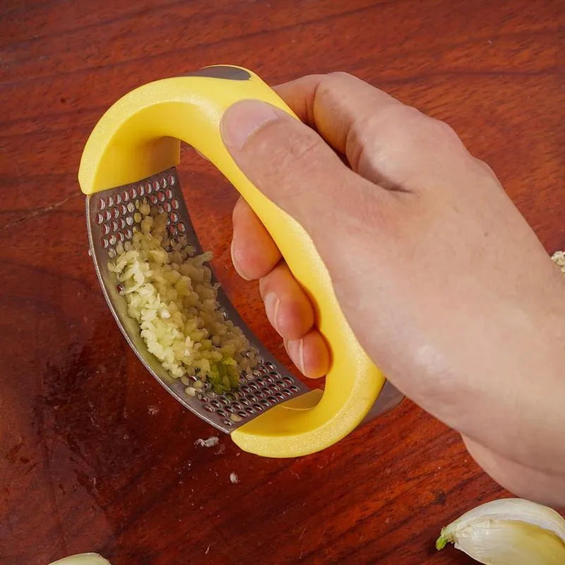 Stainless steel garlic press with ergonomic handle in assorted colours on a kitchen counter.