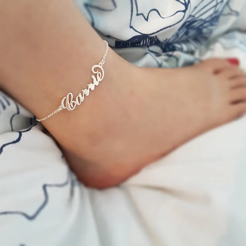 Gold titanium steel cable chain anklet with personalised name engraving on a sandy beach background