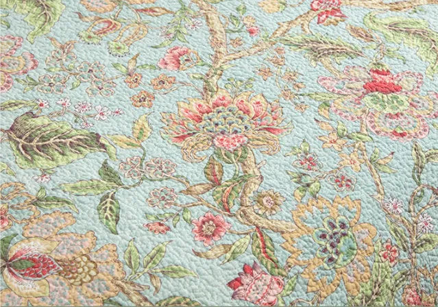 American-style floral quilted cotton bedspread in blue, shown draped on a double bed.