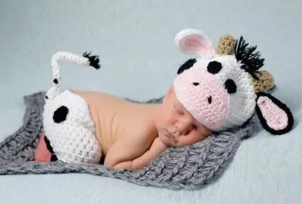 Hand-knitted white baby cow suit set with matching hat and pants on a newborn