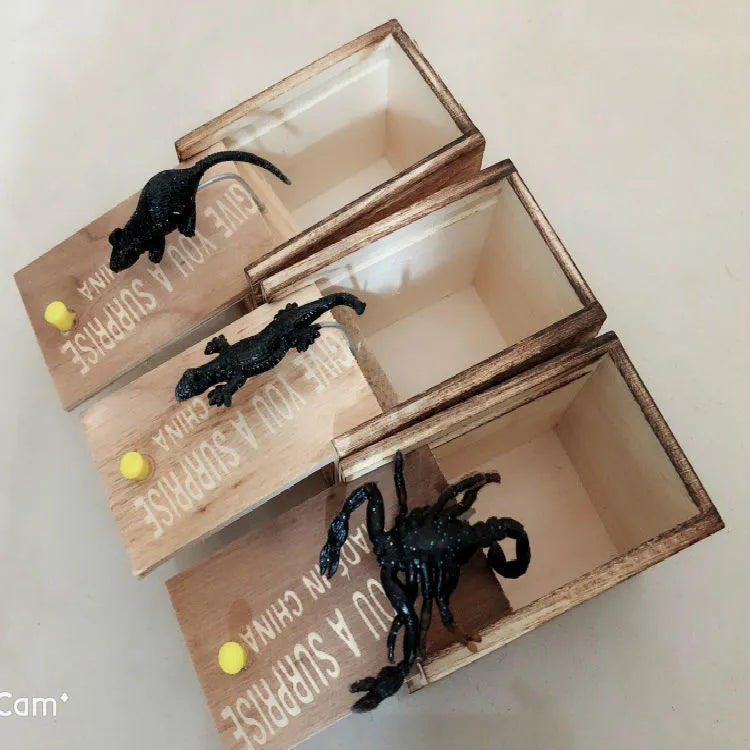 Wooden prank scare box with a lifelike spider figurine on a table.