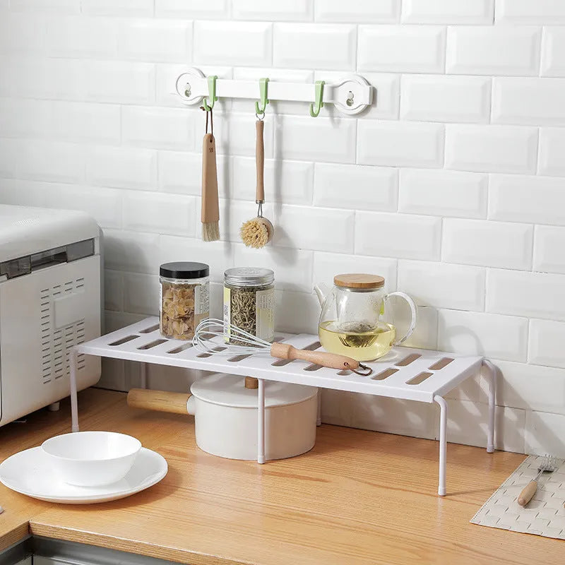 White telescopic plastic kitchen rack with single shelf, shown at adjusted height on a kitchen floor.