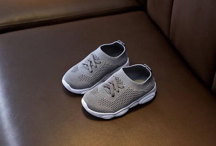 Children's white fabric lazy slip-on shoe with non-slip rubber sole on a wooden floor.