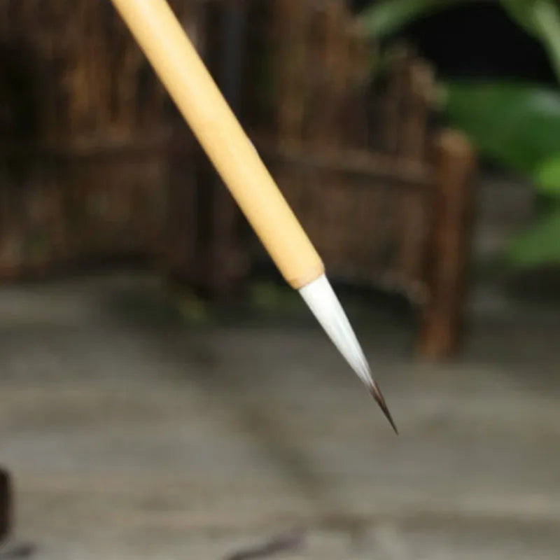 Four gold-coloured thin writing brushes with pine branch design, size 0, on a flat surface.