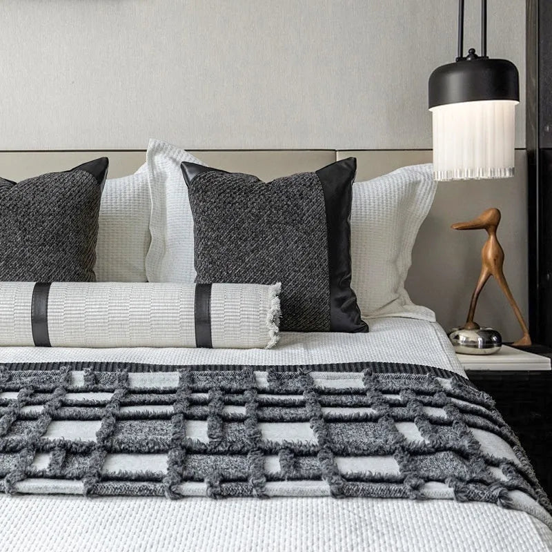 Grey and white plaid bed blanket draped over a dark grey duvet with a matching pillowcase and round leather-look cushion.