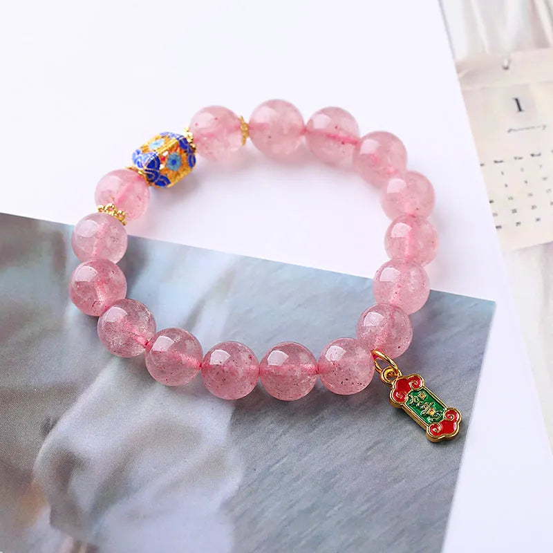 Close-up of a pink strawberry quartz crystal bracelet with hand-woven Ruyi design and letter detailing.