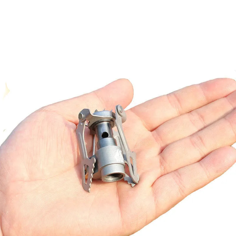Portable gas camping stove with a one-piece metal furnace body, shown on an outdoor surface.