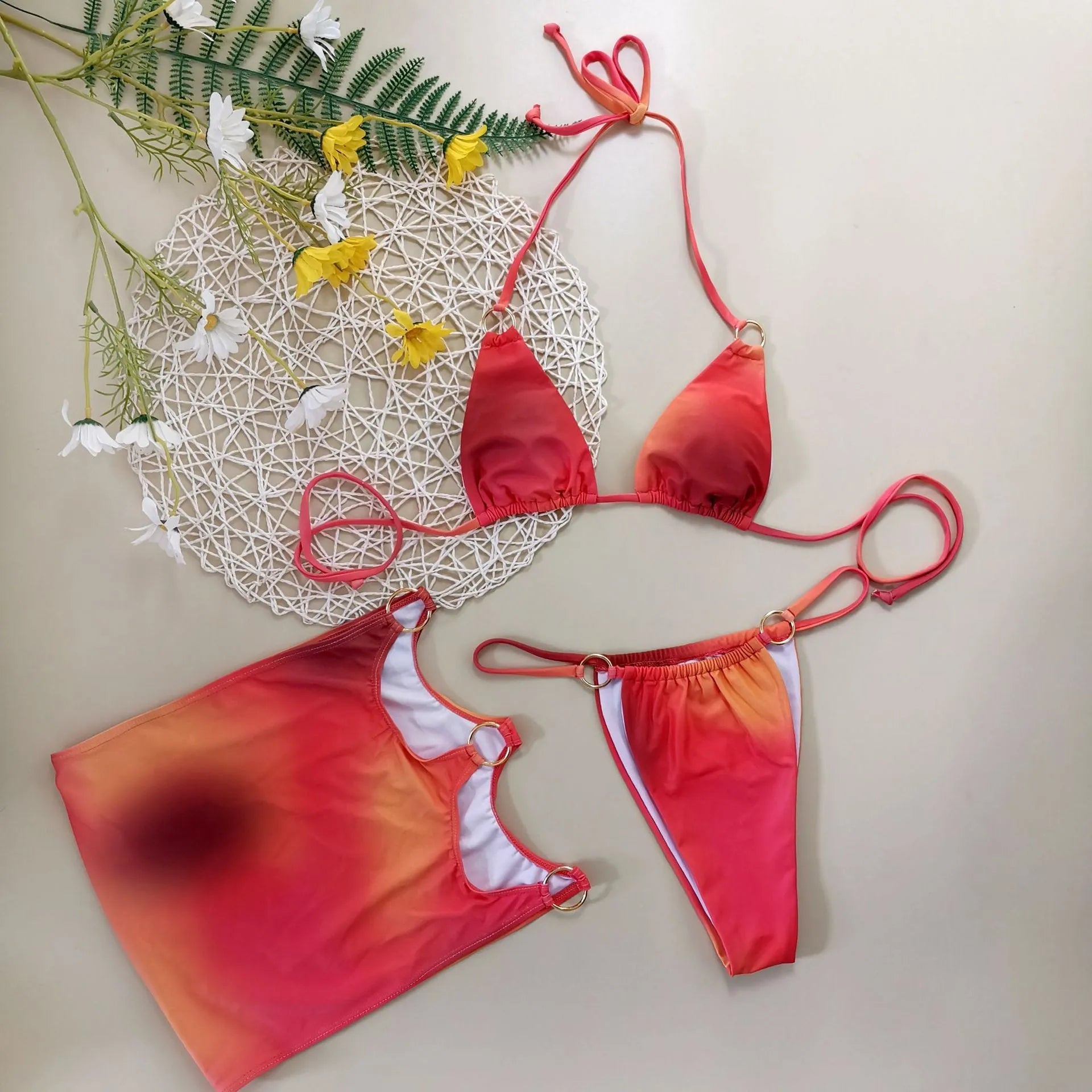 Tie-dye gradient print three-piece swimsuit set with halter top, bikini bottoms, and wrap skirt laid flat.