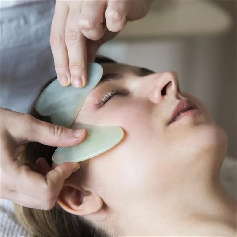 Flat natural jade gua sha stone for facial massage in green colour on white background