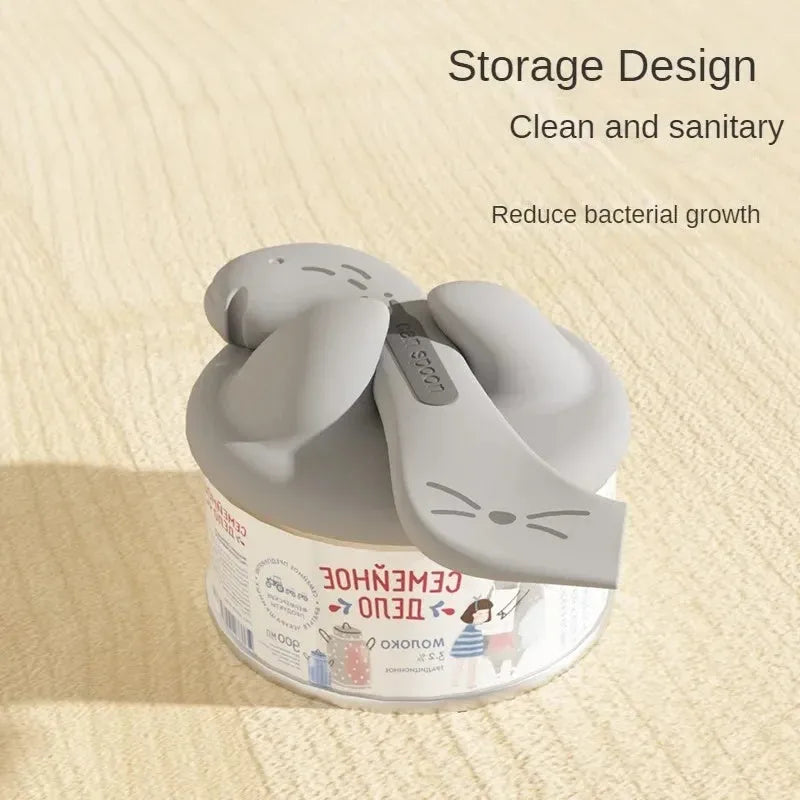 Grey silicone pet food spoon with integrated can opener and matching sealing lid for tins.