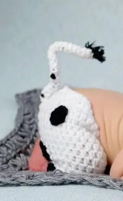 Hand-knitted white baby cow suit set with matching hat and pants on a newborn