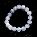 Natural white moonstone bracelet with round polished beads showing a blue sheen, laid flat.