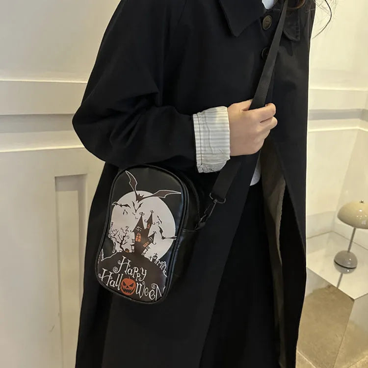 Black Halloween crossbody bag with orange pumpkin, white ghost, and bat graffiti print, shown worn across the body.