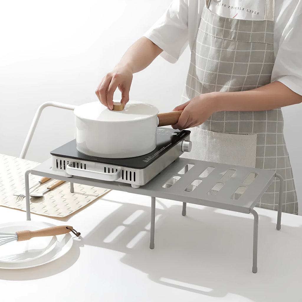 White telescopic plastic kitchen rack with single shelf, shown at adjusted height on a kitchen floor.