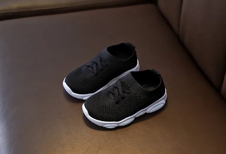 Children's white fabric lazy slip-on shoe with non-slip rubber sole on a wooden floor.