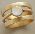 A gold-plated geometric ring with a hollow design and micro-inlaid white chalcedony details.