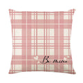 Square decorative pillow cover with red and black plaid and white heart pattern on a grey sofa.