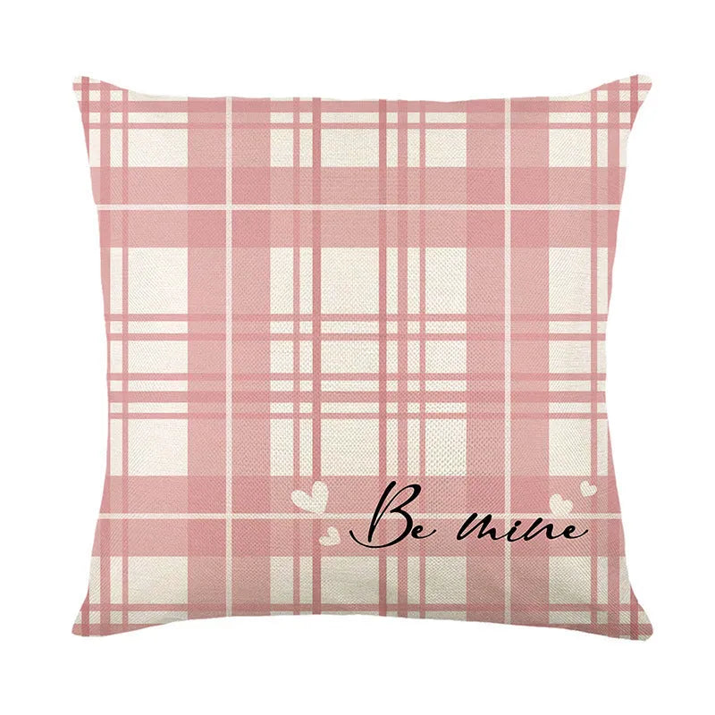 Square decorative pillow cover with red and black plaid and white heart pattern on a grey sofa.