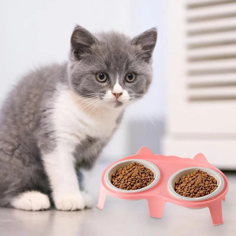 Blue ceramic cat food and water bowl set on a white stand with a hook, showing tilted feeding angle.