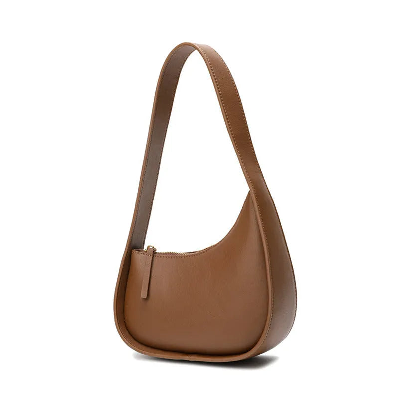 Small half moon shaped leather women's shoulder bag with a wide strap, shown in light brown.